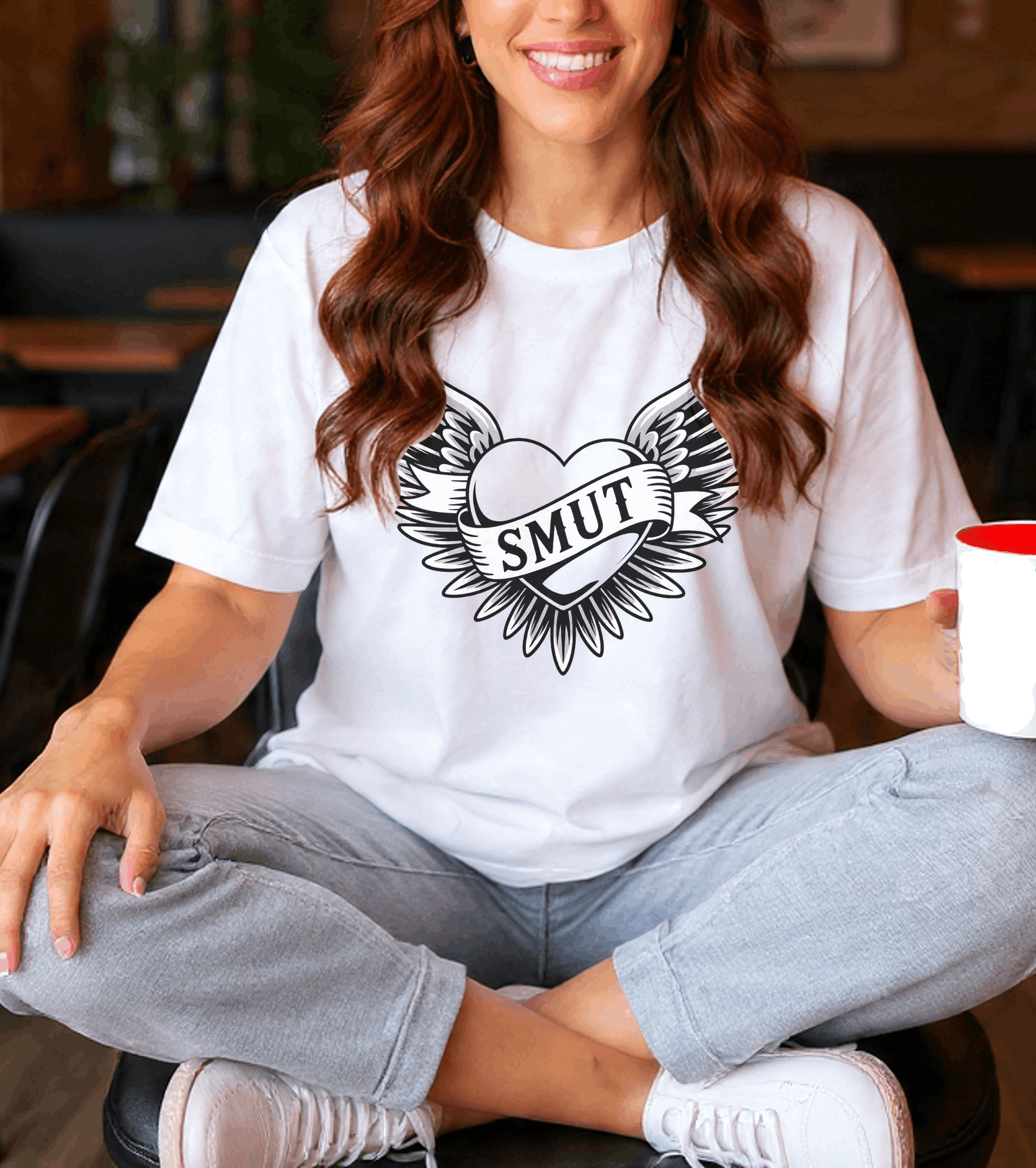 Person wearing a white t-shirt with a graphic design and holding a cup.