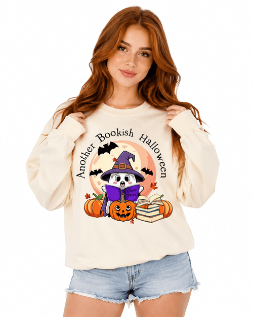 Cream unisex crewneck sweatshirt with cute illustrated witch reading a book design surrounded by pumpkins and autumn leaves, perfect for Halloween-loving readers