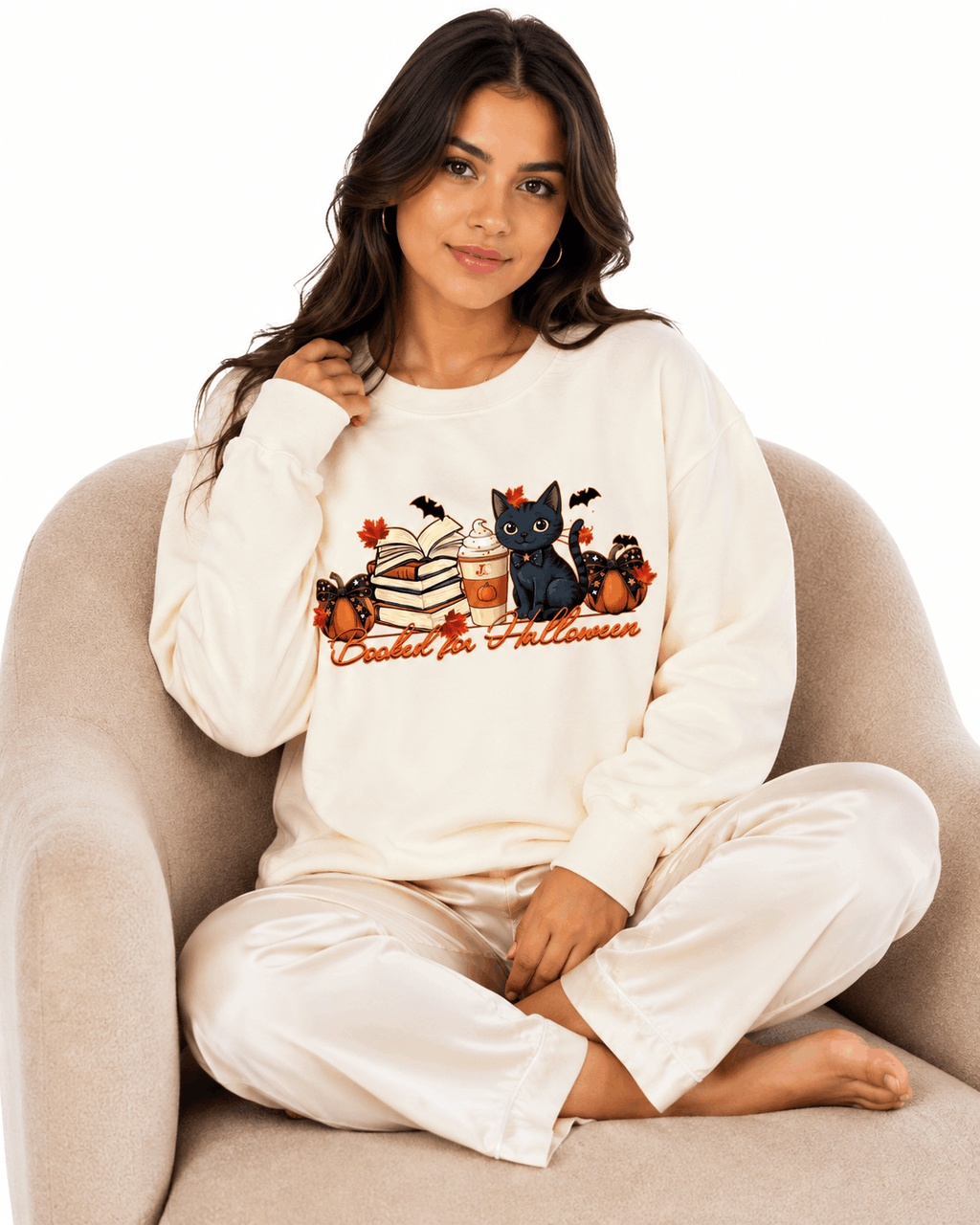 Cream unisex crewneck sweatshirt with cute black cat surrounded by books, pumpkins, coffee, and bats with "Booked for Halloween" text, perfect for cat-loving book readers