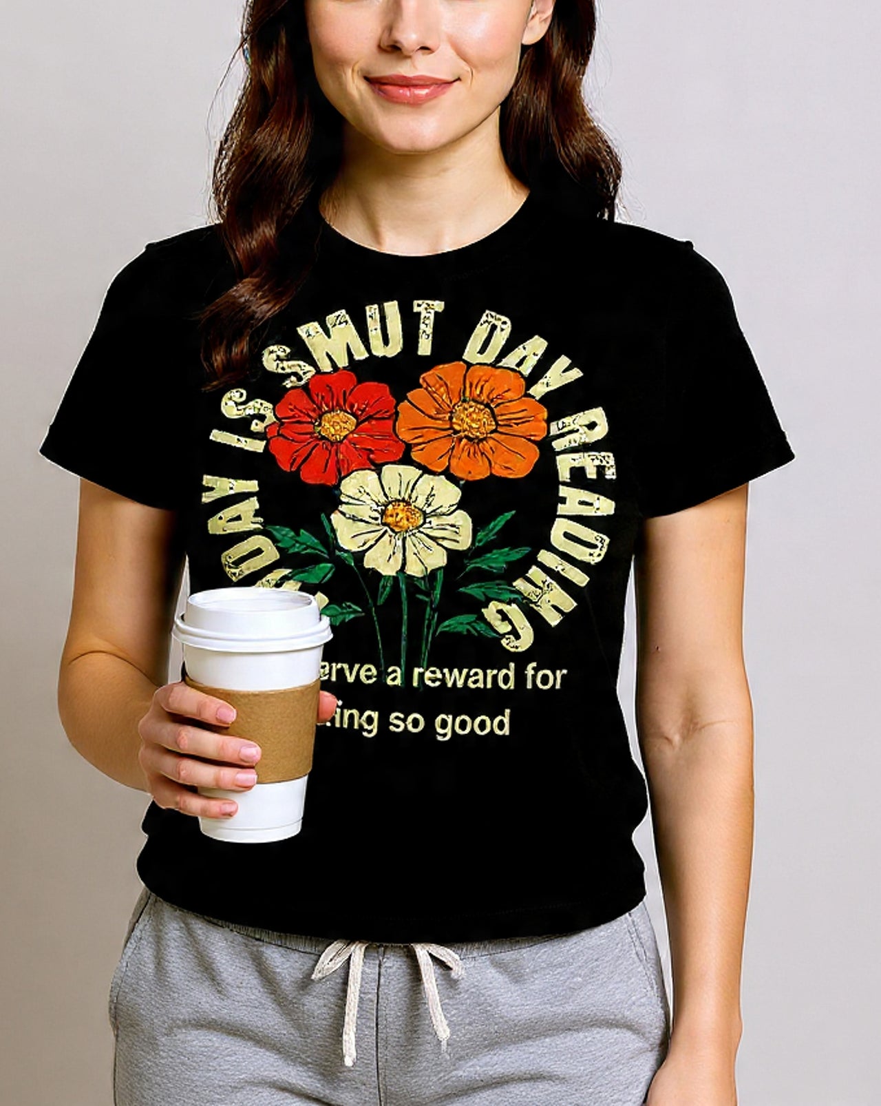 Person wearing a black t-shirt with colorful floral design and text, holding a coffee cup.