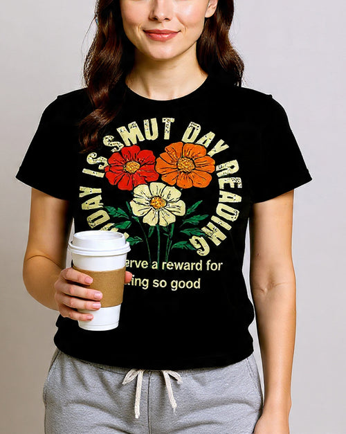 Person wearing a black t-shirt with colorful floral design and text, holding a coffee cup.