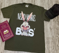Green t-shirt with cartoon character and 'Need More Books!' text on a wooden surface with a book and cap.