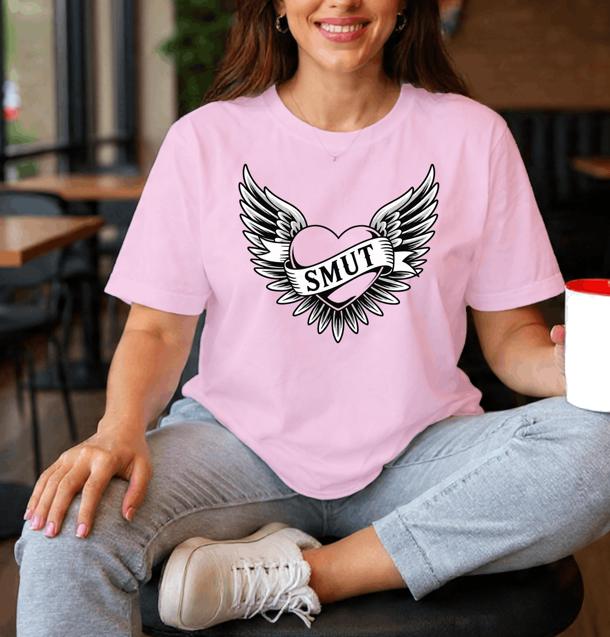 Person wearing a pink t-shirt with a graphic design and holding a Starbucks cup in a casual setting.