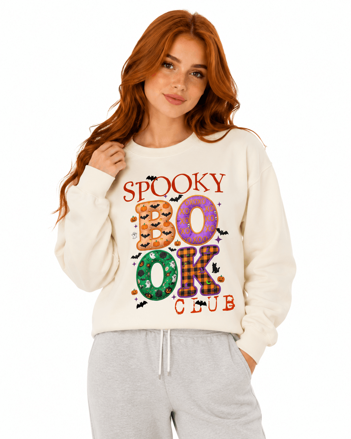 Cream unisex crewneck sweatshirt with colorful "Spooky Book Club" design featuring pumpkins, bats, and patterned letters for Halloween-loving readers