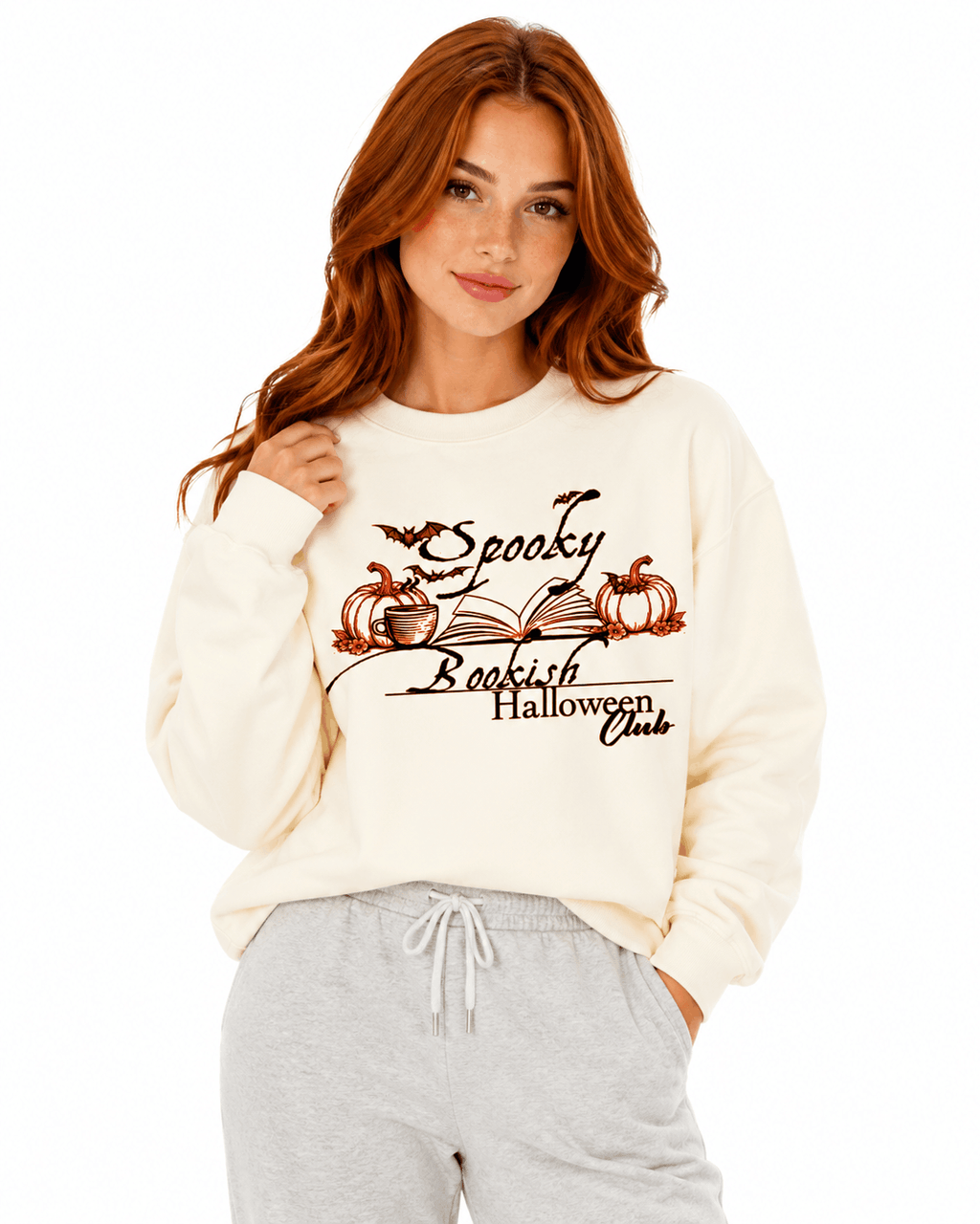 Cream unisex crewneck sweatshirt with elegant hand-drawn spooky bookish Halloween club design featuring open book, pumpkins, coffee cup, bats and leaves with calligraphy text