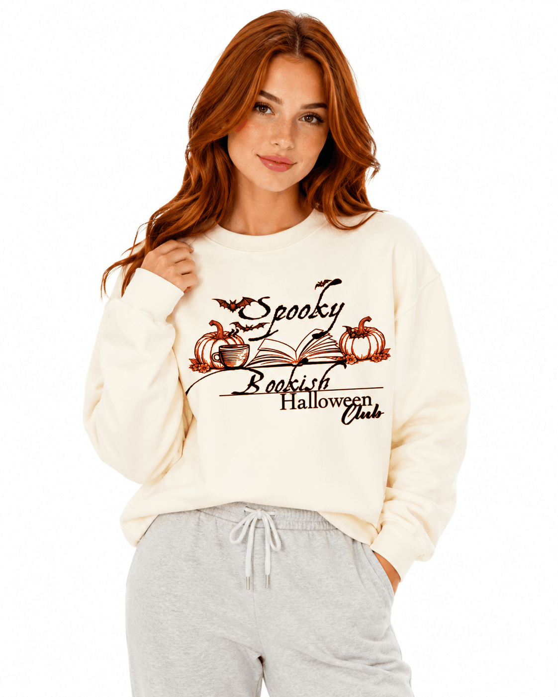 Cream unisex crewneck sweatshirt with elegant hand-drawn spooky bookish Halloween club design featuring open book, pumpkins, coffee cup, bats and leaves with calligraphy text